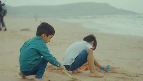 Vista-De-Perfil-De-Dos-Niños-Jugando-Con-Arena-En-La-Playa-De-Baluchistán-En-Pakistán