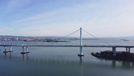 Disparo-Aéreo-De-Un-Dron-Alejándose-Lentamente-Con-El-Puente-De-La-Bahía-Al-Fondo