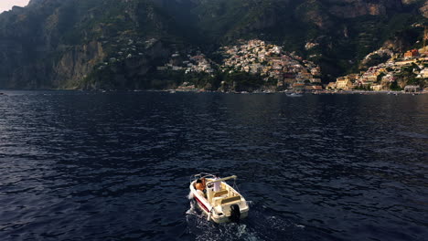 Drohnenaufnahme-Eines-Bootes,-Das-Sich-In-Richtung-Des-Dorfes-Positano-Bewegt,-Goldene-Stunde-In-Amalfi,-Italien