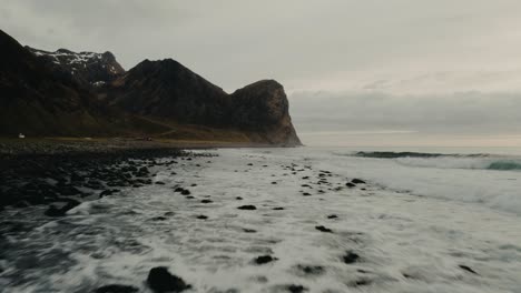 Olas-Rompiendo-En-La-Playa-Rocosa-Rodeada-De-Montañas-En-Las-Islas-Lofoten-En-Noruega-Durante-Un-Día-Nublado-Y-Colores-Grises