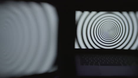 Two-computer-screens-in-a-dark-room-displaying-a-hypnotic-spiral-pattern