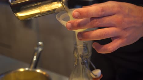 Close-up-side-view-4k-shot-on-bartender's-hands-pouring-lemon-juice-in-a-bottle-through-a-plastic-funnel