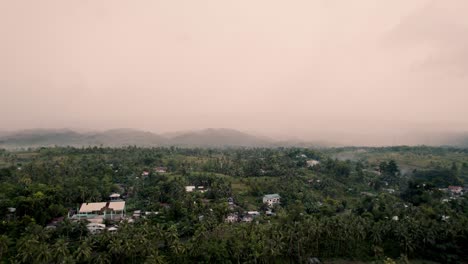Moalboal-in-the-Philippines-flying-drone-with-a-panorama-view-looking-out-over-the-jungle-with-palm-trees-and-a-small-village-with-ocean-nearby-on-a-cloudy-and-misty-day-with-cars-driving-through
