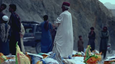 Anciano-De-Aldea-Caminando-Junto-A-Sacos-De-Ayuda-Para-La-Distribución-De-Alimentos-En-El-Suelo-En-Baluchistán