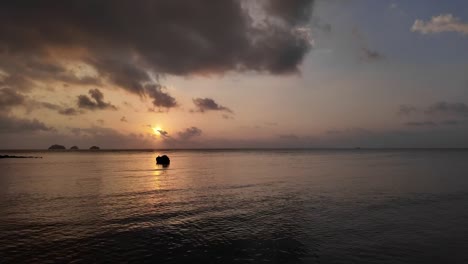 Small-boat-slowly-sails-towards-a-romantic-sunset