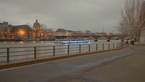 Pan-shot-of-cycling-track-around-the-River-Seine-with-tourist-boat-and-Pont-des-Arts-in-the-background