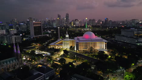 Die-Berühmte-Istiqlal-Moschee-Erleuchtet-Den-Nachthimmel-Von-Jakarta-Bei-Sonnenuntergang,-Während-Eine-Drohne-Kreist