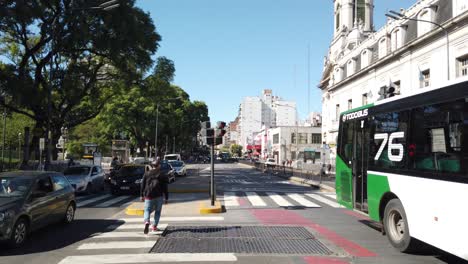 Anciano-Cruza-La-Avenida-Rivadavia-Bulliciosa-Ciudad-De-América-Latina-Parque-De-Tráfico-Hito-Urbano-De-Buenos-Aires-Argentina,-Autobuses,-Autos-Circulando-Por-El-Barrio-De-Flores,-Plaza-Pueyrredon