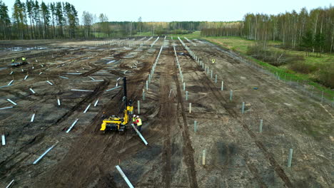 Technicians-installing-poles-at-a-solar-energy-park,-with-a-machine---Aerial-view