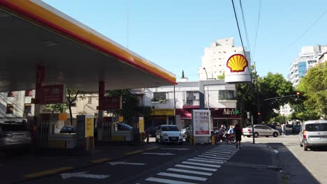 Panoramic-at-Gas-Shell-Oil-Fuel-Petrol-stations,-car-traffic,-argentina-fill-tank-in-recharge-energy-company,-buenos-aires-streets-town-in-daylight