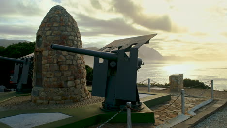 Hermanus,-Goldener-Sonnenaufgang-über-Walker-Bay-Mit-Blick-Auf-Das-Historische-Kriegsdenkmal-Mit-Steinhaufen-Und-Zwei-Marinegeschützen
