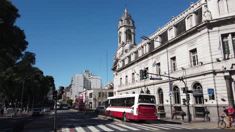 Banco-Nacional-De-Buenos-Aires-Bandera-Argentina-En-La-Avenida-Rivadavia-Tráfico-Centro-De-Arquitectura-Histórica-En-El-Barrio-De-Flores,-Basílica-Y-Plaza-Verde-Urbana-De-Pueyrredon,-Parque