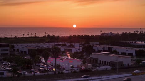 Drone-Hyperlapse-of-the-Carlsbad,-California-In-N-Out-Burger-location-during-sunset-with-the-Pacific-Ocean-and-steady-flow-of-vehicles-through-the-drive-thru-lane