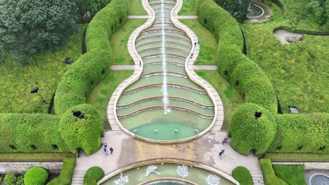 Drone-Shot-of-Alnwick-Gardens,-England-UK,-Cascade-Fountain-and-Green-Fields-60fps