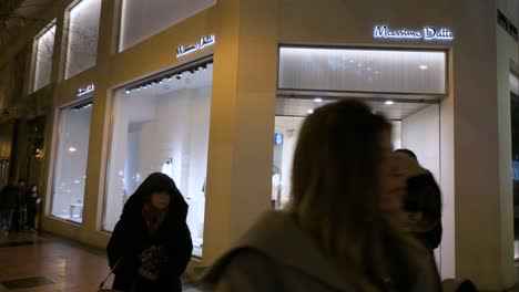 Los-Peatones-Y-Compradores-Pasan-Por-La-Tienda-De-Fabricación-De-Ropa-Española-Y-Marca-Massimo-Dutti-Durante-La-Noche-En-Madrid,-España