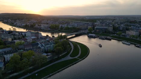 Wide-drone-shot-filmed-at-sunset-in-Krakow-Poland-over-the-Vistula-River-with-a-slight-haze-in-the-sky-diffusing-the-sun-as-cars-drive-over-a-bridge