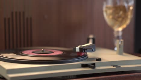 Beginnen-Sie-Mit-Der-Wiedergabe-Einer-Vinyl-Schallplatte-Auf-Einem-Grammophon-Aus-Den-1970er-Jahren-Mit-Einem-Glas-Wein-Im-Hintergrund