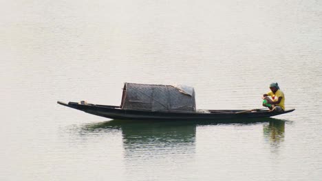 Fisherman-sitting-on-board-of-Traditional-Asian-boat,-navigating-Surma-river