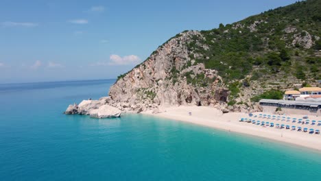 Luftaufnahme-Des-Wunderschönen-Sandstrandes-Mit-Sonnenschirmen-Und-Sanftem-Türkisfarbenem-Meeresrauschen-In-Der-Sommersaison-Am-Kathisma-Strand-Auf-Der-Insel-Lefkada