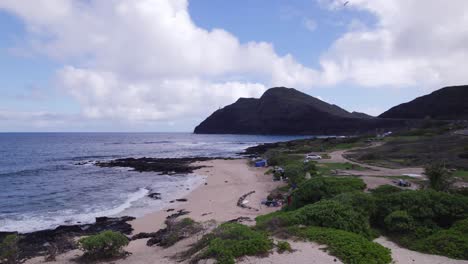 drone-footage-along-a-sandy-Hawaiian-beach-on-the-island-of-Oahu-as-ocean-waves-roll-calmly-to-shore-with-lush-greenery-lining-the-secluded-beach