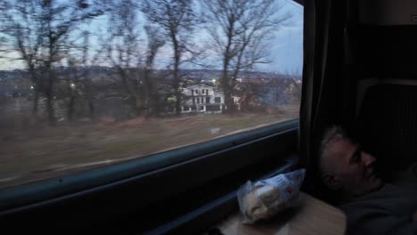 Train-ride-through-village-close-to-Iasi-in-Romania,-old-man-sleeping