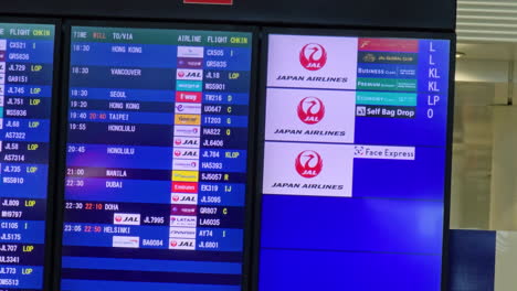 Man-walking-past-a-modern-flight-timetable-at-the-Narita-Airport-in-Tokyo,-Japan