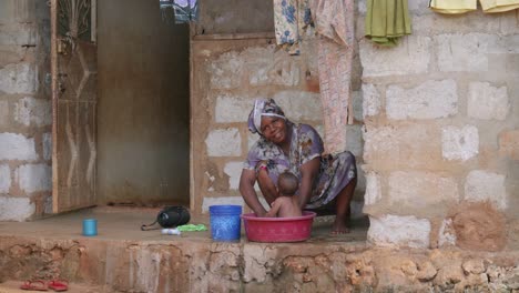 Tanzania-Madre-Bañando-A-Su-Bebé-En-La-Cuenca-En-El-Suelo-Fuera-De-Casa-En-El-Porche