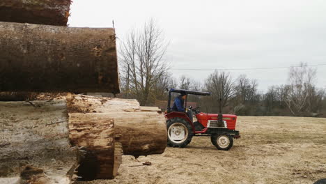 Trabajador-En-Un-Aserradero-Conduciendo-Un-Tractor-Yanmar-M1610d-Rojo-Tirando-De-Una-Pila-De-Tablas