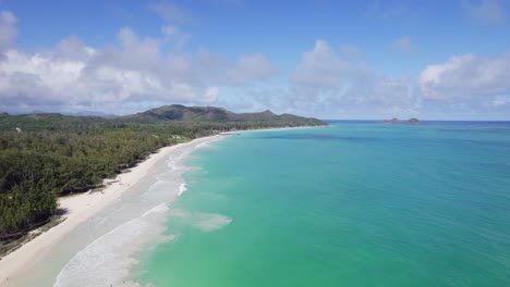 turquoise-water-meets-white-sand-and-lush-green-mountains-in-this-drone-footage-of-paradise-with-blue-sky-and-puffy-white-clouds-on-the-island-of-Oahu-Hawaii