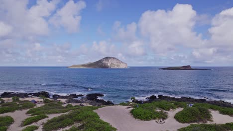 stationary-shot-of-two-small-volcanic-formation-islands-off-the-coast-of-Oahu-Hawaii-in-the-Pacific-Ocean-with-sandy-beach-with-greenery-in-the-foreground