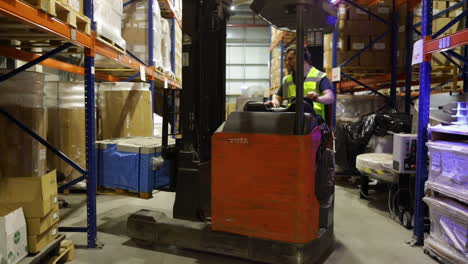 Factory-warehouse-worker-in-safety-vest-operates-forklift-to-arrange-pallets-of-goods
