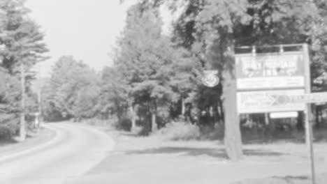 Vintage-Black-and-White-Footage-of-a-Quiet-Street-with-Billboard-and-Trees-in-US