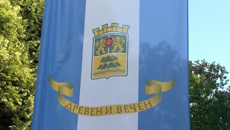 Close-up-of-the-flag-and-Coat-of-arms-of-Plovdiv-against-a-tree-and-the-sky