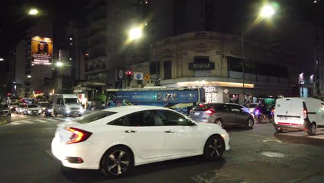 Police-officers-riding-motorcycles-with-blue-lights-at-night-in-Buenos-Aires-traffic-vibrant-latin-city,-policeman-controlling-transit-at-Avenue-Rivadavia,-nighttime,-commercial-stores-around