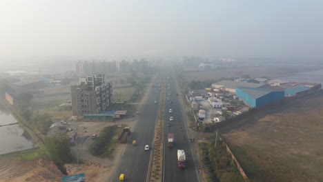 aerial-drone-view-drone-camera-moving-backwards-showing-traffic-and-vehicles-on-the-highway-and-large-factories-and-fields-on-the-side