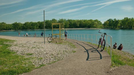 Capture-the-vibrant-atmosphere-of-Zagreb's-Jarun-Lake-on-a-sunny-day,-with-parked-bicycle-and-people-enjoying-the-tranquil-lakeside-setting-in-this-stable-footage