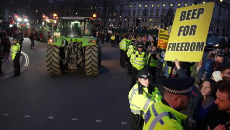 Un-Manifestante-Sostiene-Un-Cartel-Que-Dice-“bip-Por-La-Libertad”-Mientras-Un-Convoy-De-Tractores-Llega-A-La-Plaza-Del-Parlamento-Al-Anochecer-Y-Una-Fila-De-Policías-Mantiene-A-La-Gente-Fuera-De-La-Carretera