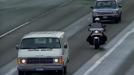 POLICE-BIKE-WITH-LIGHTS-ON-CHASING-VAN-ON-HIGHWAY-DURING-DAY