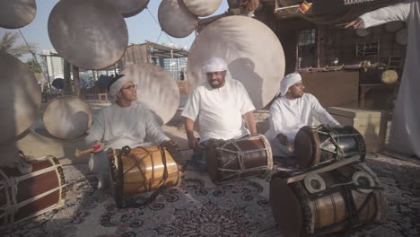 Handmade-drums-made-by-local-Emirati-locals-while-he-is-teaching-little-kids-how-to-play-drums,-Drums-for-celebrating-heritage-and-cultural