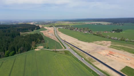 Vista-Aérea-De-La-Carretera-En-Construcción-En-Medio-De-Campos-Verdes