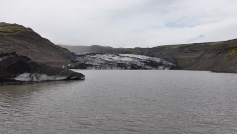 Drone-Shot-of-Glacier-and-Glacial-Lagoon-in-Moody-Landscape-of-Iceland-on-Cloudy-Summer-Day-60fps