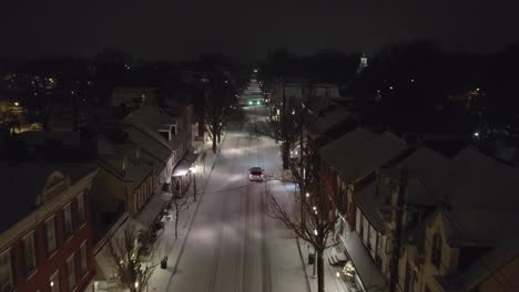 Aerial-footage-of-car-driving-through-the-small-town-of-Lititz-PA-on-a-snowy-winter-evening,-going-east