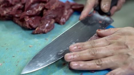 Chef-expertly-and-skillfully-cutting-fresh-raw-red-meat-with-a-sharp-knife-on-a-blue-plastic-cutting-board