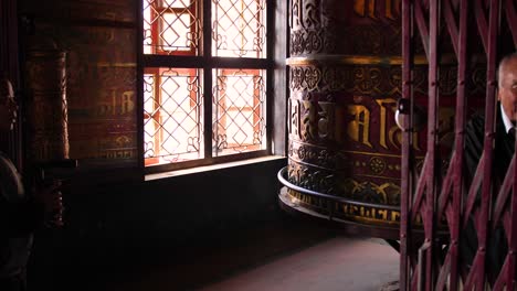 Large-prayer-wheel-spinning-with-people-on-the-outer-edge-of-Boudhanath-Temple,-Kathmandu,-Nepal