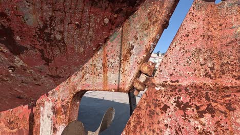 Engine-propeller-and-rudder-of-thick-rusty-metal-of-old-fishing-boat-stranded-in-harbor-to-be-repaired-and-tuned,-sunny-day,-close-up-shot-traveling-downwards
