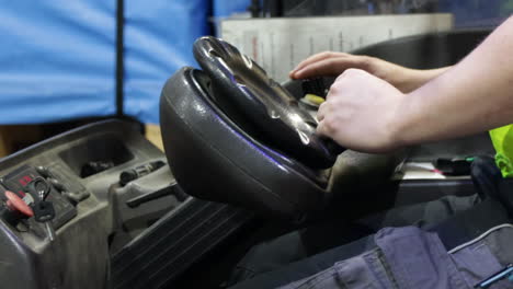 Warehouse-worker-in-safety-vest-leans-against-forklift-steering-wheel-pressind-buttons