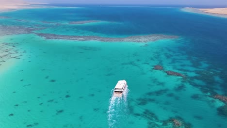 Aerial-of-a-tourist-boat-gracefully-glides-over-the-turquoise-waters-of-the-Blue-Lagoon-in-Dahab,-Egypt,-embodying-the-concept-of-leisurely-exploration-and-serene-natural-beauty