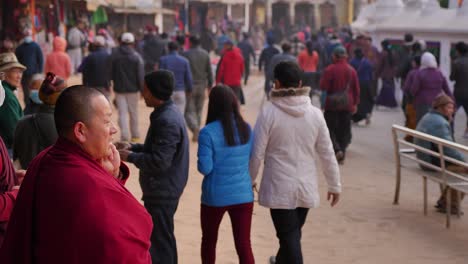 Ground-level-close-shot-of-Buddhist-Monk-watching-people-walk-around-the-outer-section-of-Boudhanath-Temple,-Kathmandu,-Nepal