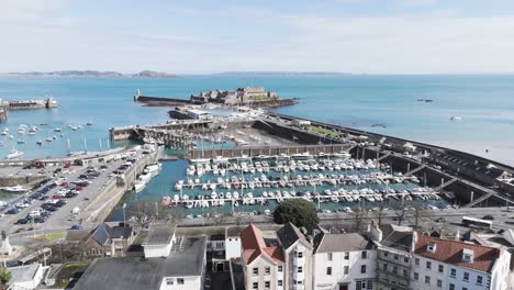 Flight-over-roof-tops-of-St-Peter-Port-Guernsey-out-over-harbour-to-Castle-Cornet-with-views-of-Herm,Jethou-and-Sark-on-clear-bright-day-with-calm-sea