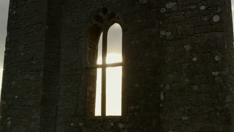 Aerial-dolly:-Medieval-Irish-Abbey-tower-backlit-by-sun,-window-glows